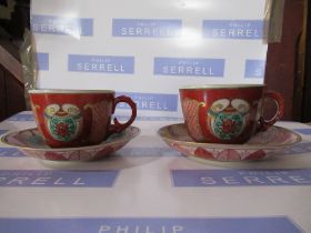 Two Oriental porcelain tea cups and saucers, decorated with panels to the a red ground, with