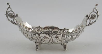 A white metal oval basket, with embossed decoration and scroll handles, raised on four feet,