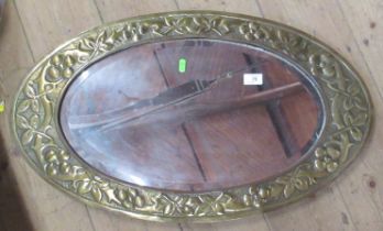 An Arts and Crafts style brass framed oval mirror, with foliate decoration and bevelled plate,