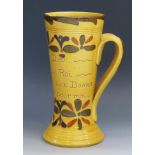 A Torquay pottery twin handled mug, inscribed with flowerhead decoration to a yellow ochre ground,