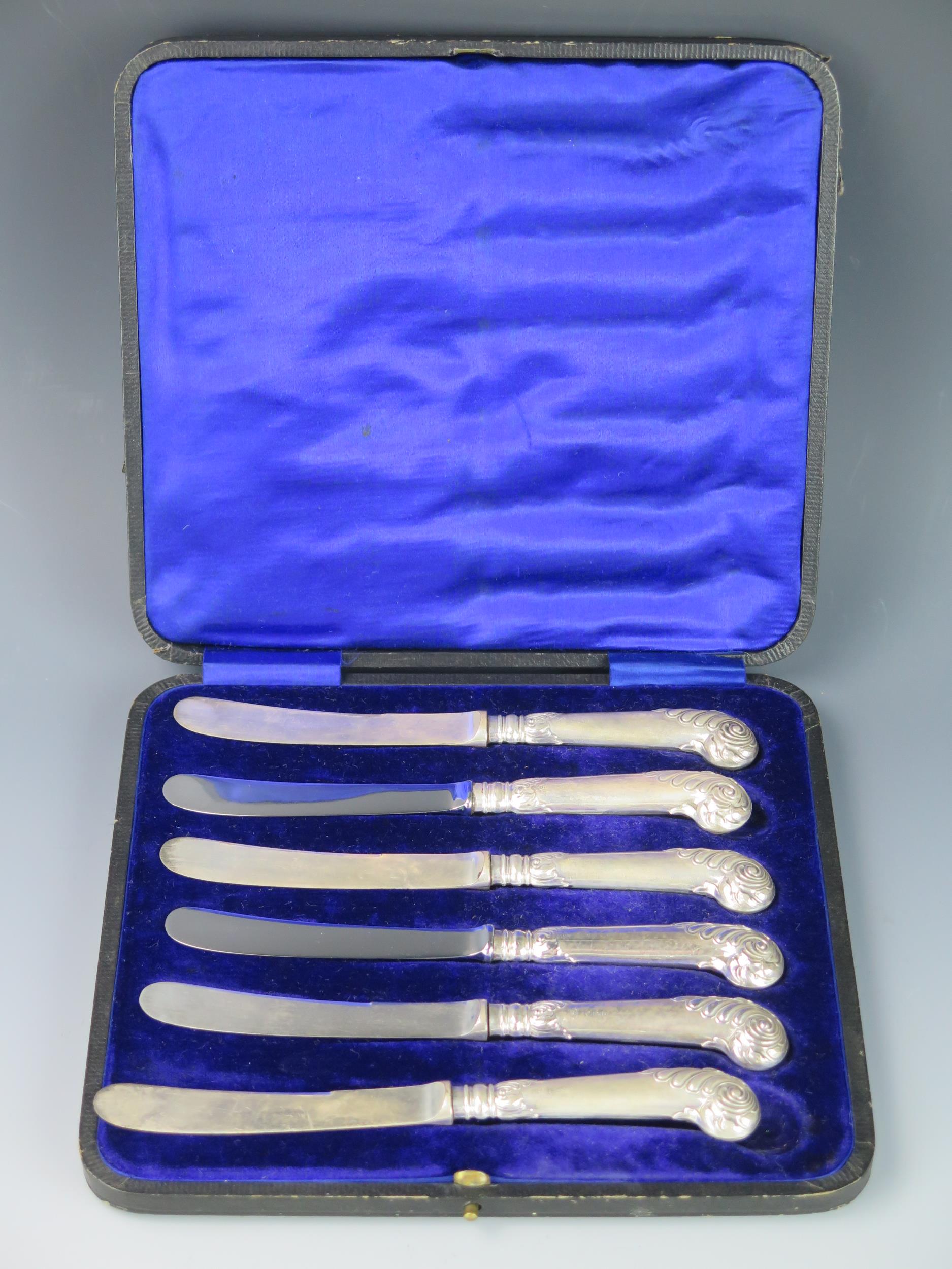 A set of six silver pistol handled butter knives with steel blades contained in a fitted case,