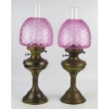 A pair of brass oil lamps with pink glass shades, circular squat reservoirs raised on reeded columns