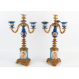 A pair of French ormolu and porcelain three branch candelabra, with urn-shaped sconces on foliate