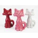 Three Dartmouth Pottery cat money boxes in red, pink and grey glazes, each 22cm high.