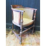 An Edwardian mahogany elbow chair of tub-shaped outline with cane panel back, sides and seat, raised