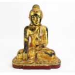 A carved hardwood, gilded and paste set model of Buddha, seated cross-legged wearing traditional