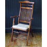 A stained beech folding elbow chair, with arched top rail and slat back, having a gross point wool