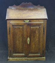 An antique oak bureau, with sloping hinged fall, and a pair of panelled cupboard doors below, on a