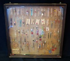 A collection of fishing floats, trout flies, and lures mounted in a glazed display case. 90 x 90cm.