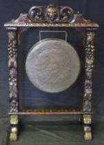 A Victorian bronze gong mounted in a heavily carved oak frame with lion mask and fruit decoration on