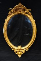 A Gilt wall mirror with oval mirror plate enclosed by a floral decorated frame surmounted by