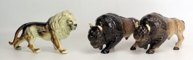 A pair of Melba Ware Buffalo, each 26cm long, together with a pottery figure of a lion, 26cm long.(