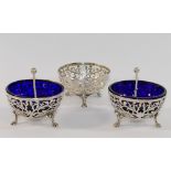 Three Edwardian bowl-shaped silver salts with pierced decoration and raised on three feet, (one blue