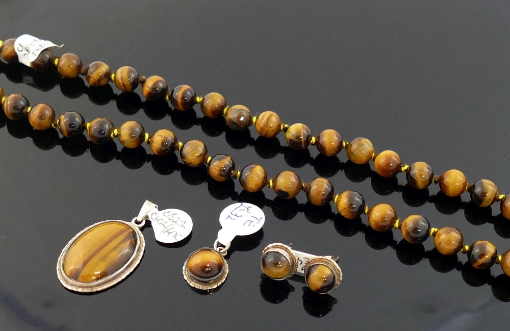 A selection of tiger's eye jewellery comprised of a string of cylindrical beads, a round cabochon