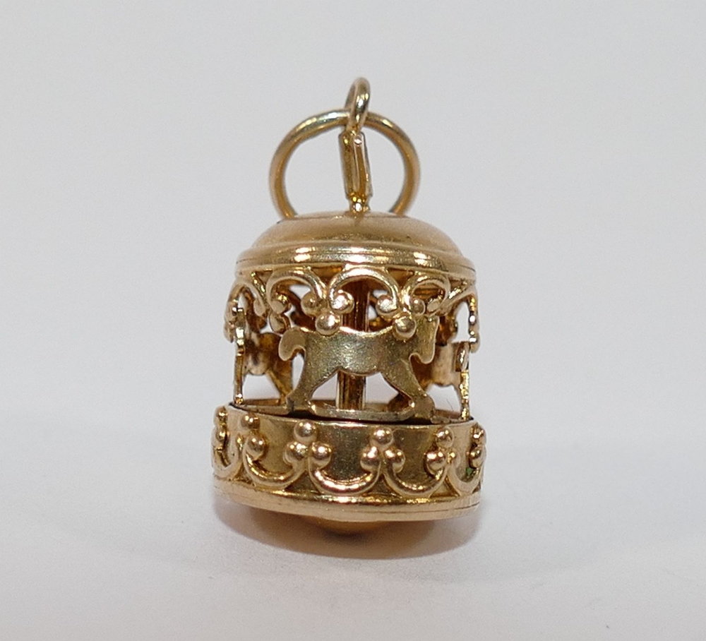 A yellow metal four-section puzzle ring, finger size V1/2, a yellow metal merry-go-round charm and a