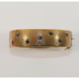 A 9 carat gold hollow hinged sapphire set bangle, with engine turned decoration, the seven round