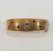 A 9 carat gold hollow hinged sapphire set bangle, with engine turned decoration, the seven round