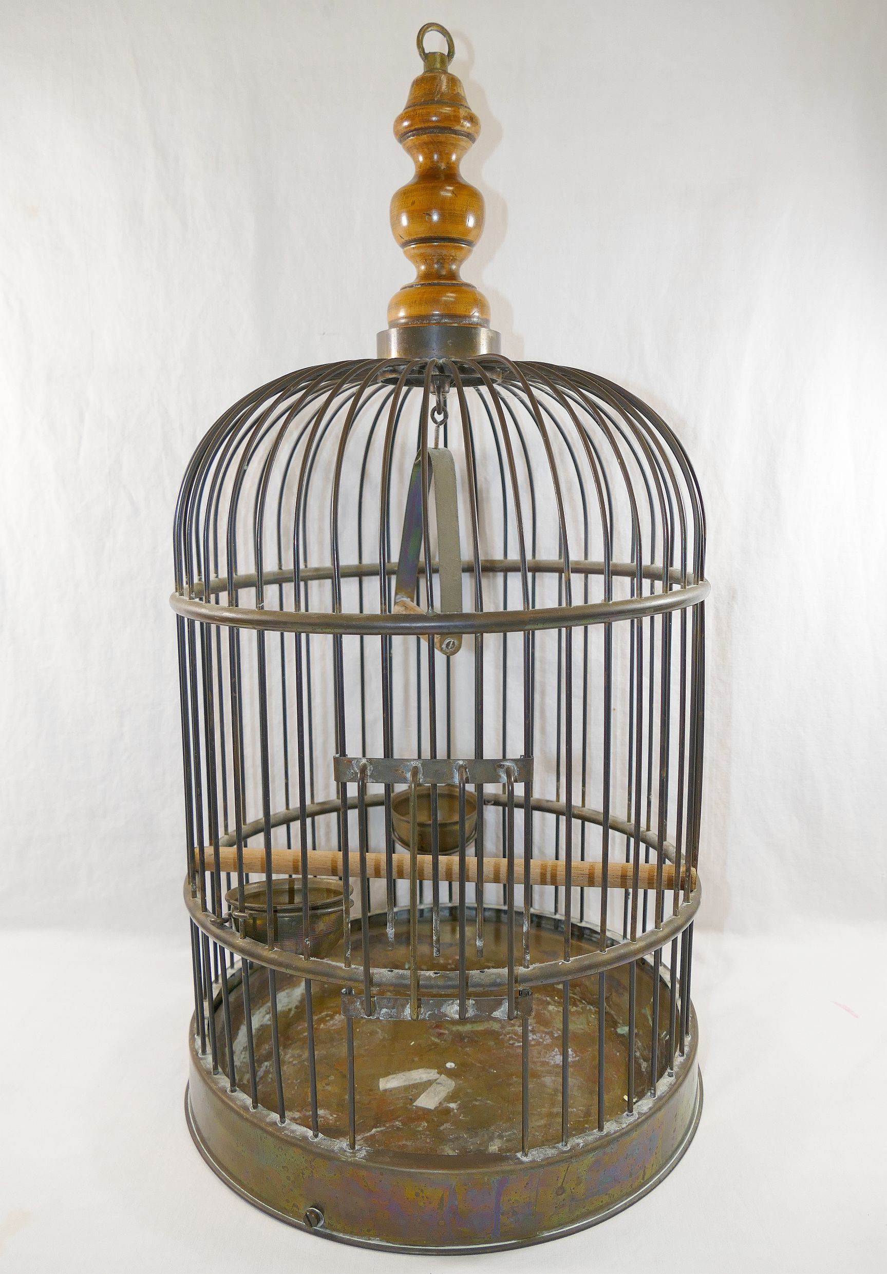 A brass bird cage, with turned wooden surmount, with wooden perch, swing, two feeding bowls and