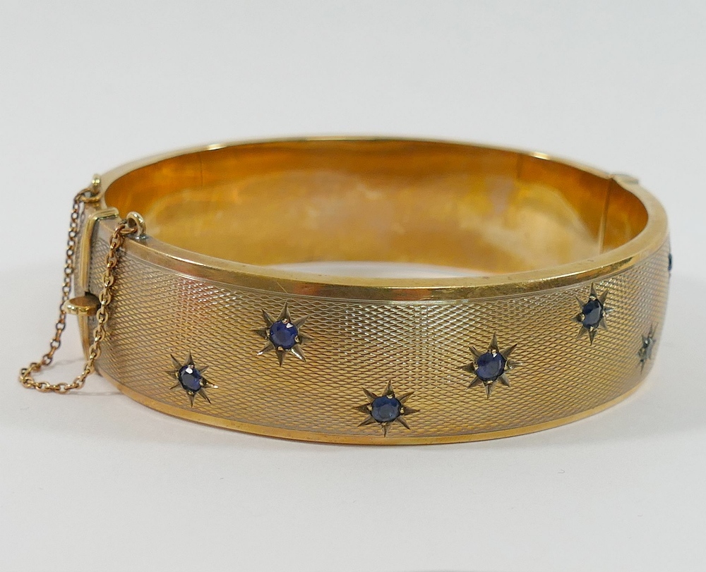 A 9 carat gold hollow hinged sapphire set bangle, with engine turned decoration, the seven round - Image 2 of 3