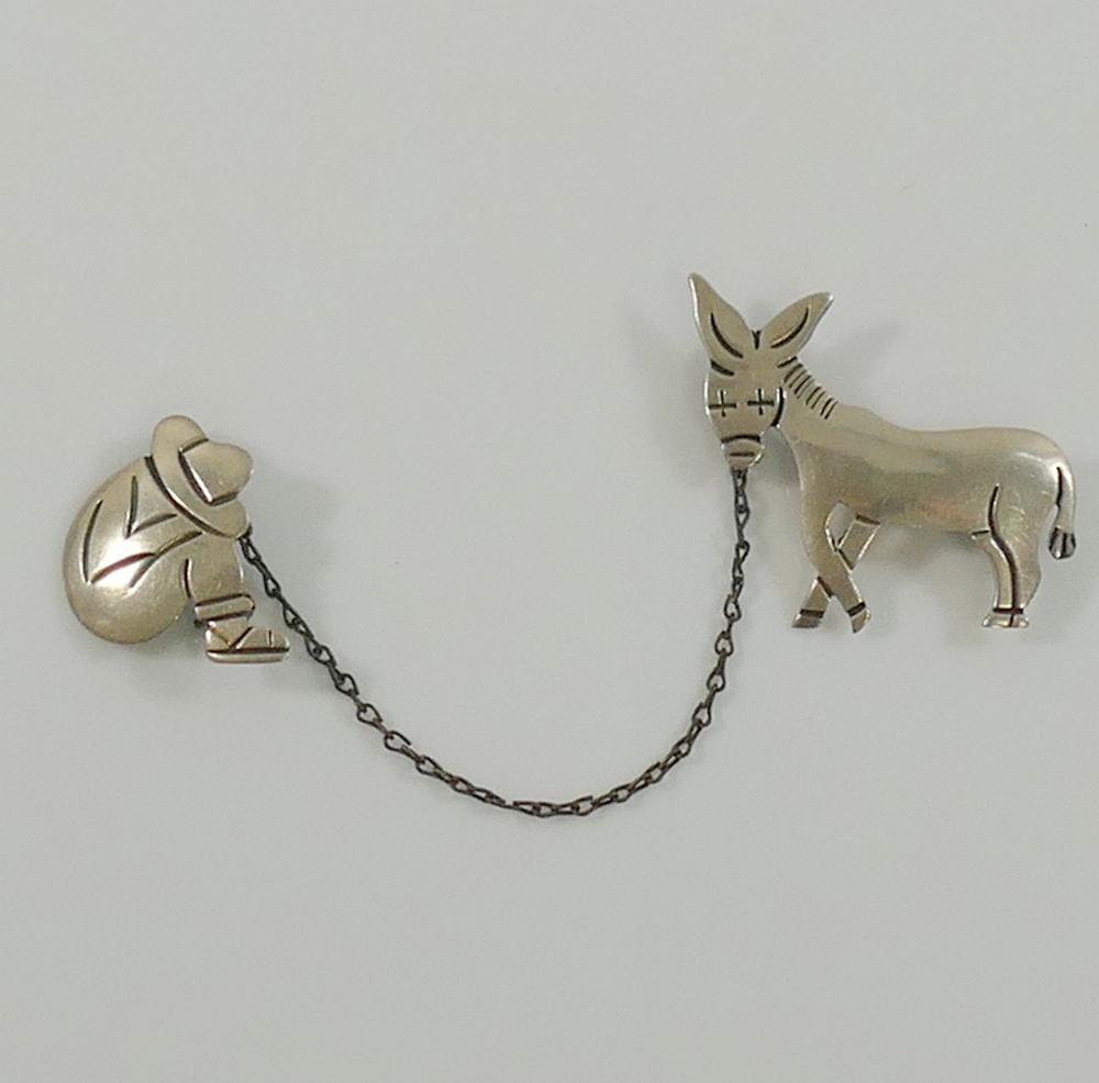 A Mexican Maricela two-part brooch of a donkey and his sleeping owner, joined by a chain, stamped '