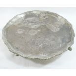 A George V circular silver tray, with shaped and gadrooned rim, raised on four hoof feet, London