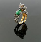 An emerald and diamond dress ring in the form of a cat with ruby eyes holding a ball in the form