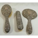 A four piece silver backed dressing table set, comprised of a hand mirror, two brushes and a