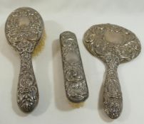 A four piece silver backed dressing table set, comprised of a hand mirror, two brushes and a