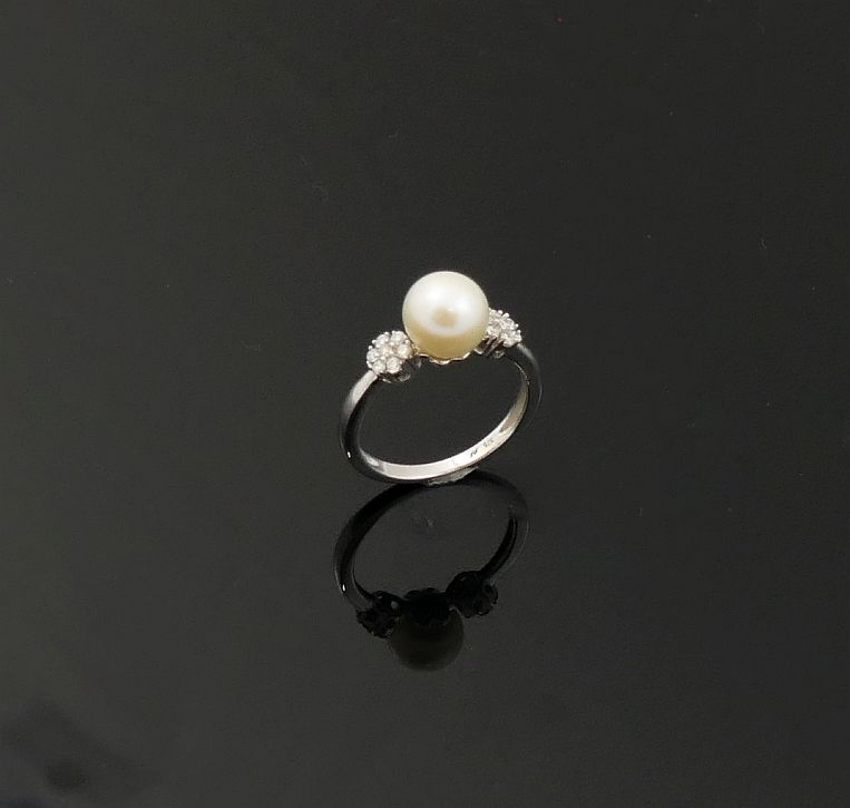 A cultured pearl and diamond ring, the central white pearl 8.15mm circumference, flanked on either