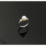 A cultured pearl and diamond ring, the central white pearl 8.15mm circumference, flanked on either