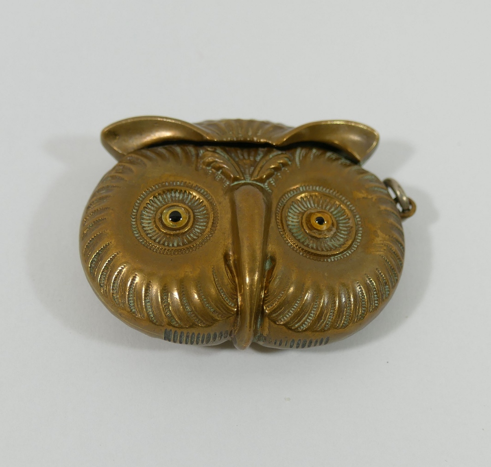 A novelty brass vesta in the form of the head of an owl, with amber glass eyes and match strike to