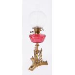 A Victorian Gothic style oil lamp, with ornate brass base, cranberry glass reservoir and glass