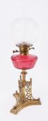 A Victorian Gothic style oil lamp, with ornate brass base, cranberry glass reservoir and glass