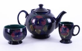 A William Moorcroft teapot decorated with Pansy's together with milk jug and sugar bowl (3).