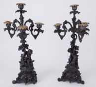 A pair of metal ornate three branch and four light candelabra decorated with cherub upon a goat,