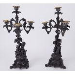 A pair of metal ornate three branch and four light candelabra decorated with cherub upon a goat,