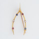 A yellow gold 'wishbone' shaped brooch set with round cut rubies, sapphires & diamonds, length