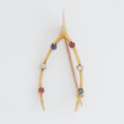 A yellow gold 'wishbone' shaped brooch set with round cut rubies, sapphires & diamonds, length