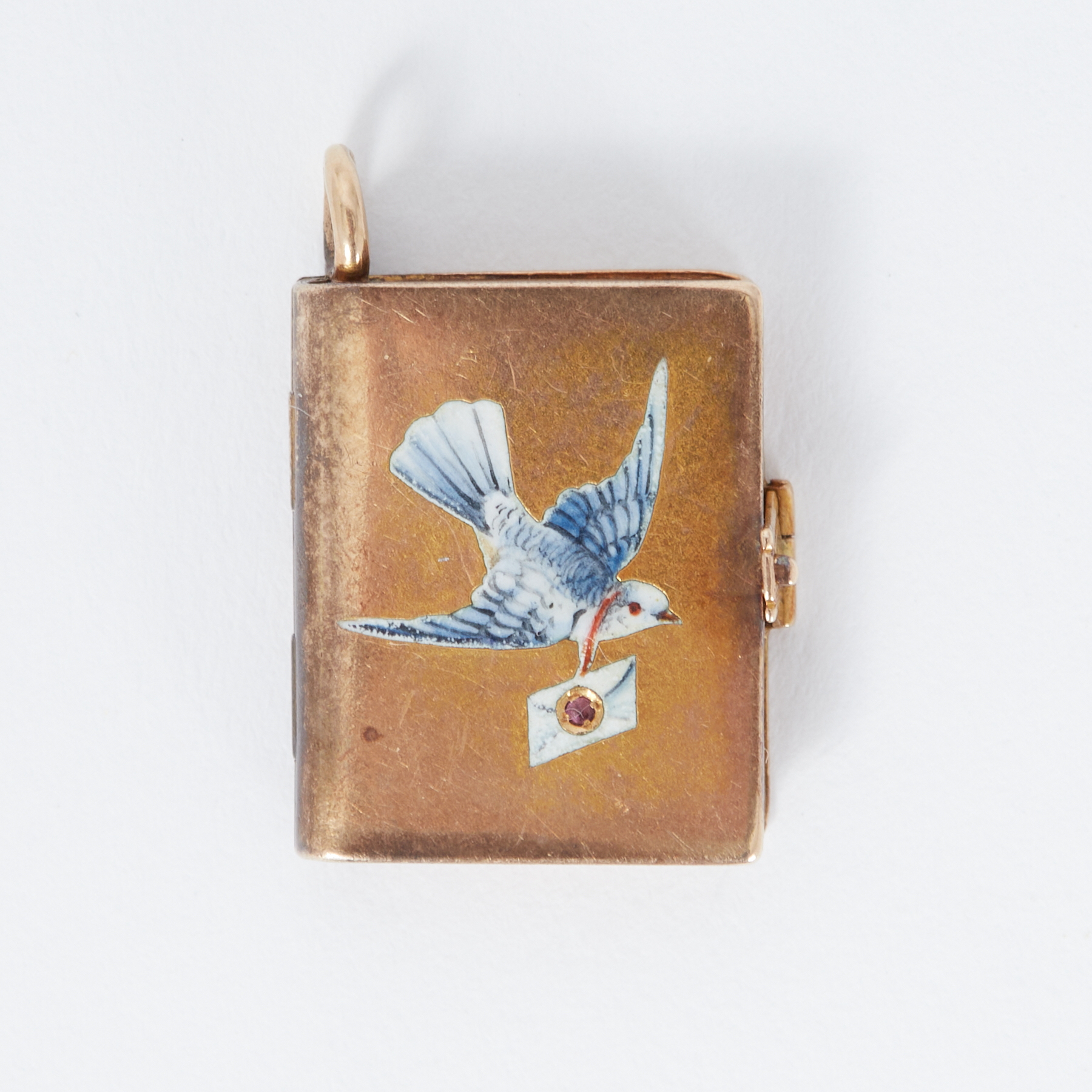 A gold locket in the shape of a book inset with a Dove & envelope set with a small ruby, measuring