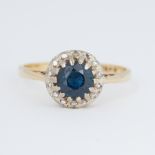 An 18ct yellow & white gold ring set with a central round cut sapphire surrounded by small round cut