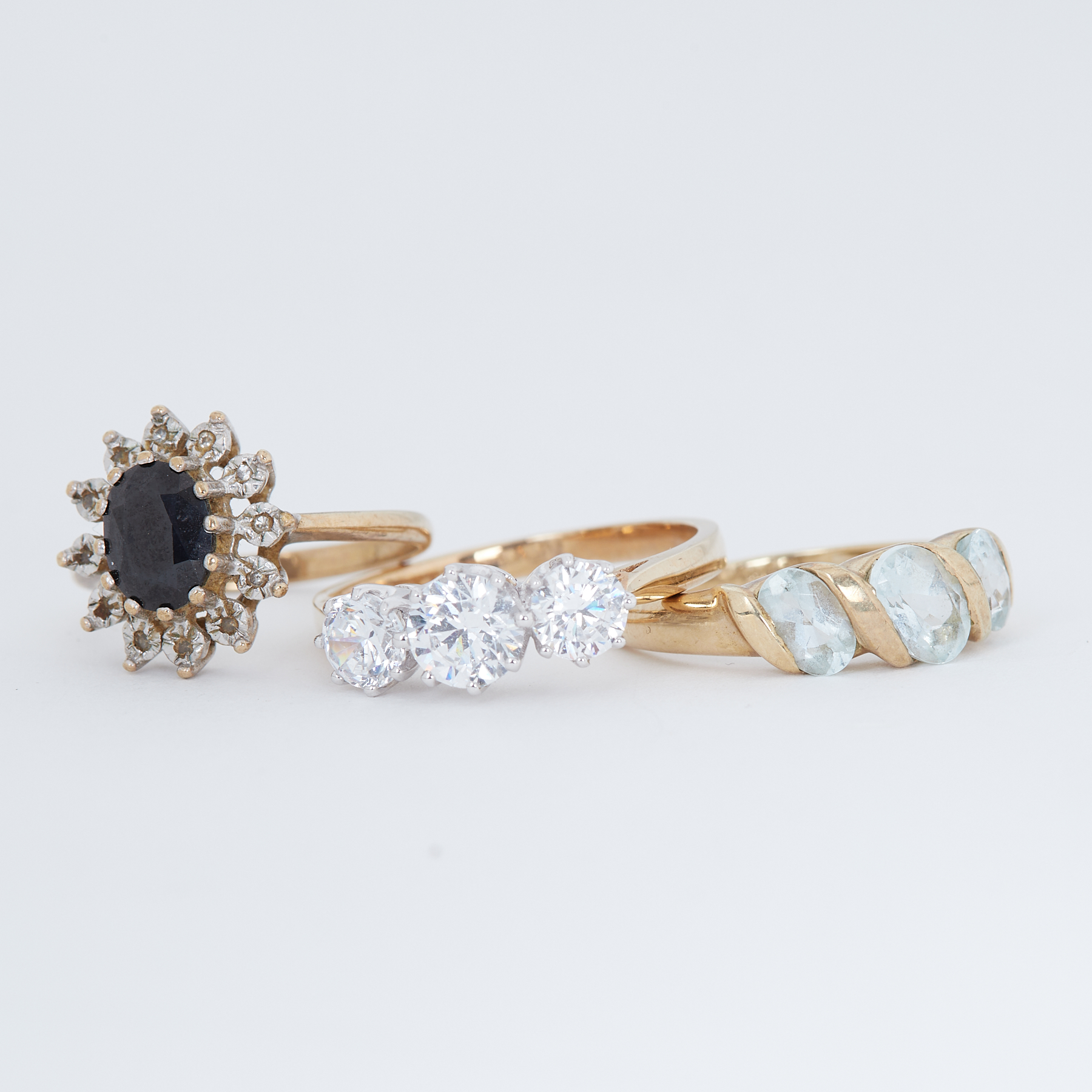 Three 9ct yellow gold rings to include a sapphire cluster ring, three stone crystal set ring & a