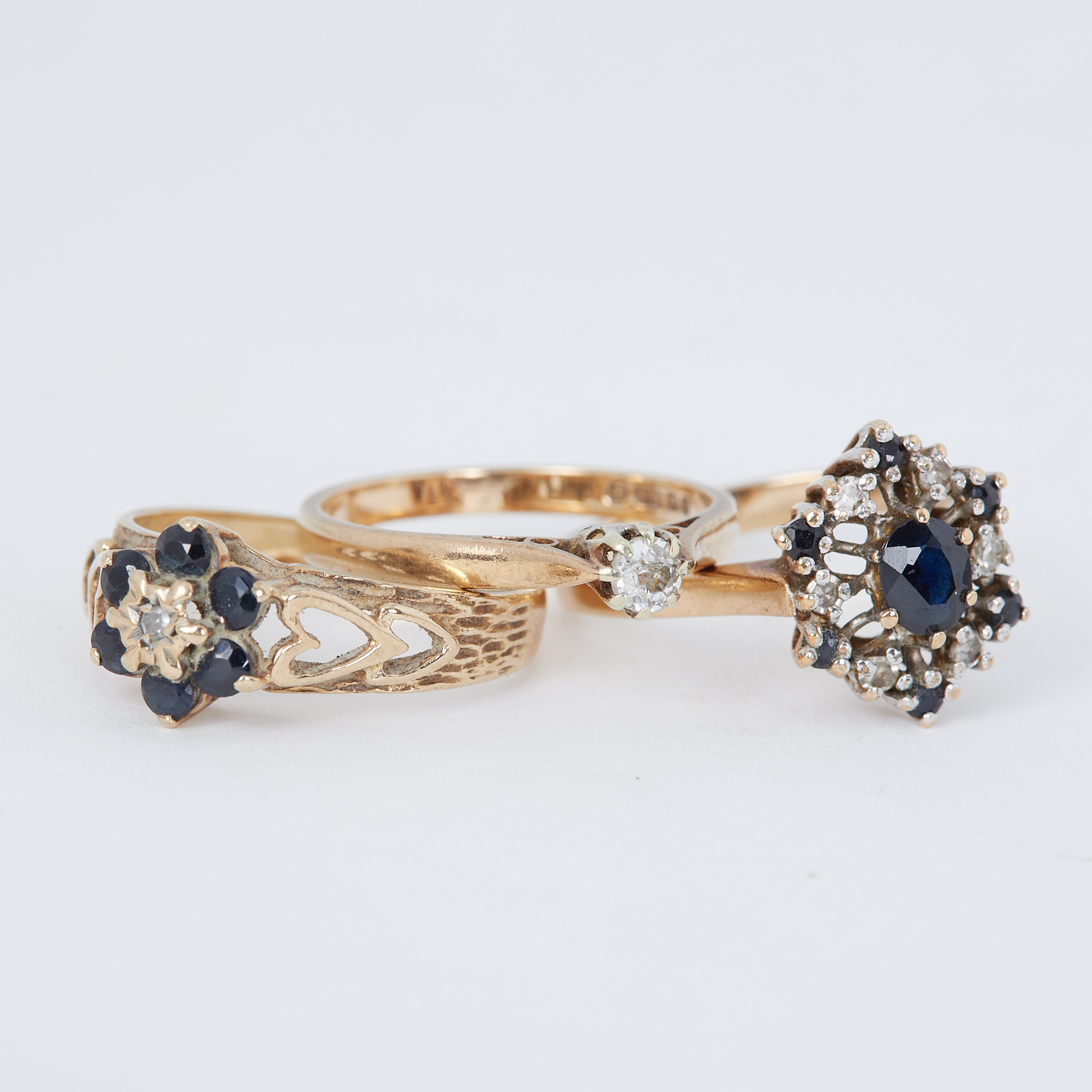 Three 9ct yellow gold rings to include a small diamond solitaire ring and two dark blue sapphire &