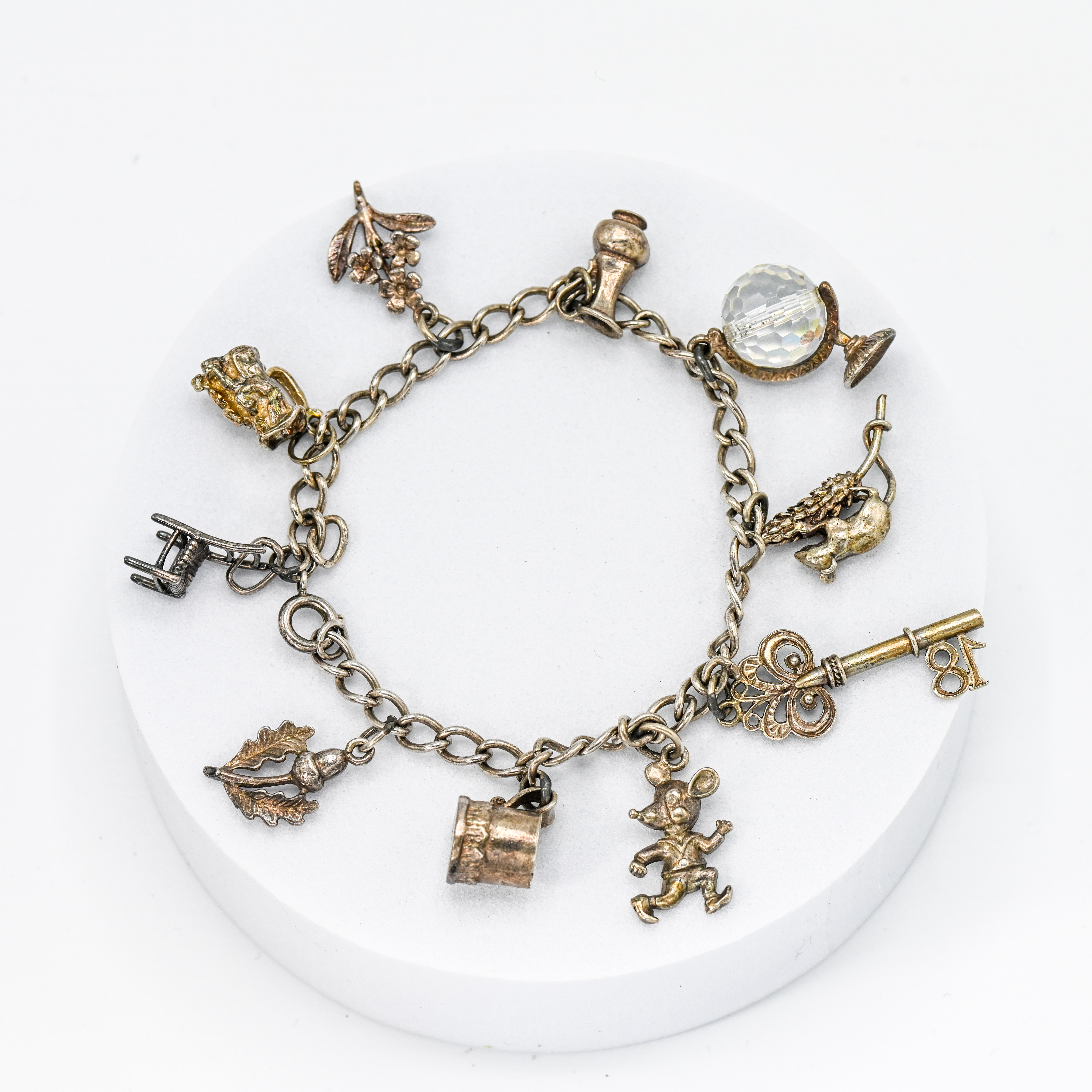 A silver charm bracelet with ten silver charms to include a chair, flowers, key, mouse, tankard,