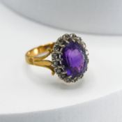 An 18ct yellow & white gold cluster ring set with an oval cut amethyst surrounded by small single
