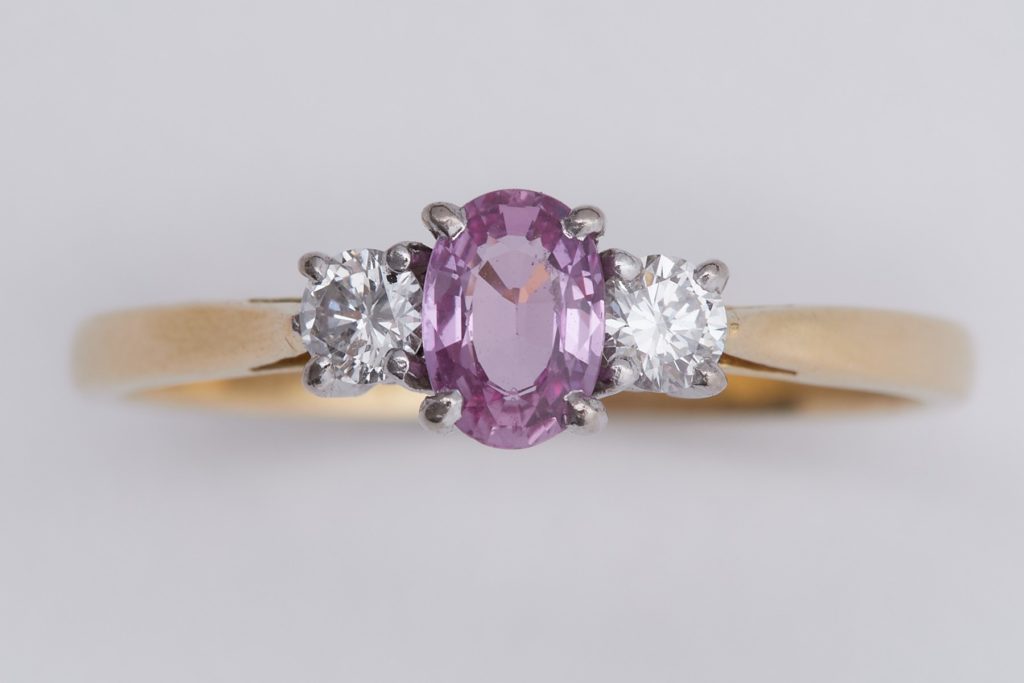 An 18ct yellow & white gold three stone ring set with a central oval cut pink sapphire