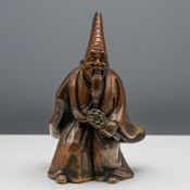 A Japanese earthenware figure of a priest, the hunched bearded figure modelled wearing a long robe