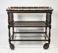 An oak two tiered dinner trolley with a glass top and cane work tier and drop sides together with