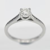 A platinum diamond solitaire ring with channel set shoulders, set with one round brilliant cut