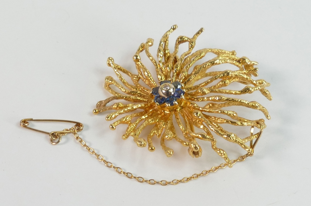 Higher carat gold designer style brooch set with blue stones surrounding a central white stone. Un