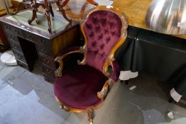A Victorian walnut button back armchair having ornate carved decoration